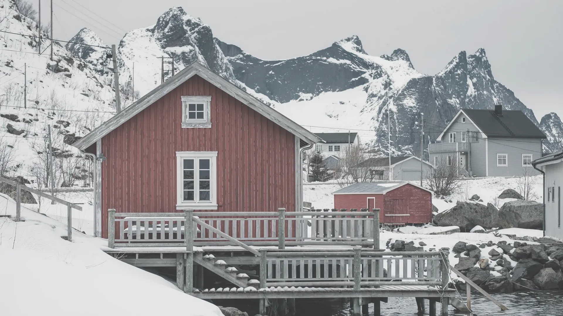 Ein einzelnes rotes Holzhaus an einer verschneiten Küste zwischen Bergen