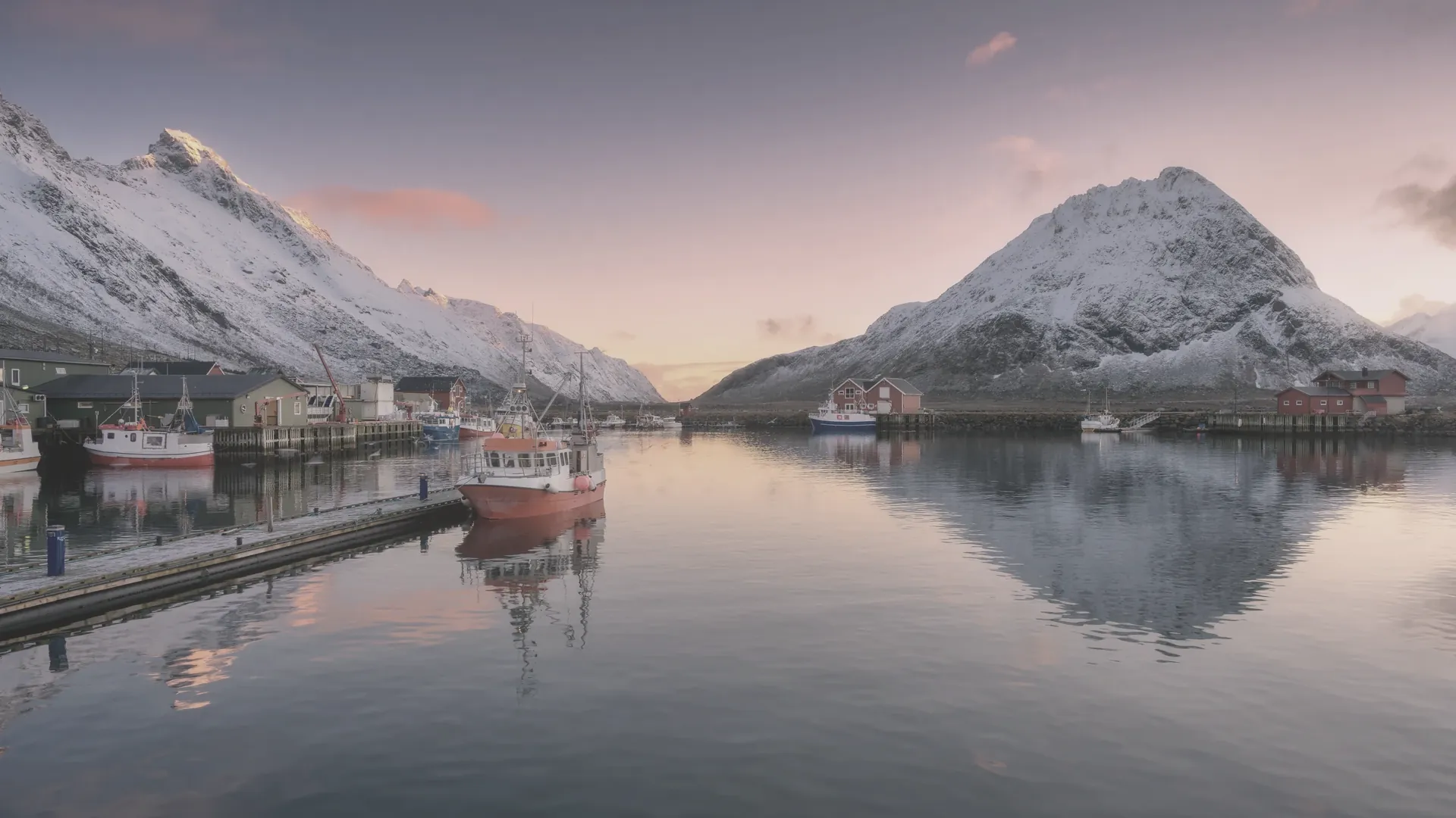 Zwei Boote an einem Steg, dahinter Schneeberge im Dämmerlicht